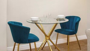 A dining area with a round glass table and two blue velvet chairs with gold legs. - Monk Bar Garden Hideaway (York)