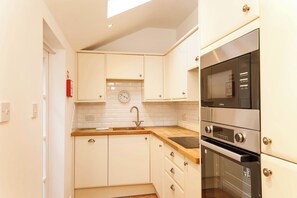 A compact kitchen with white cabinets, a wooden countertop, a sink, and a built-in oven. - Monk Bar Garden Hideaway (York)
