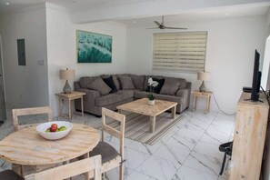Un salon moderne avec un canapé d’angle, une table de salle à manger ronde en bois et un téléviseur posé sur un meuble en bois.