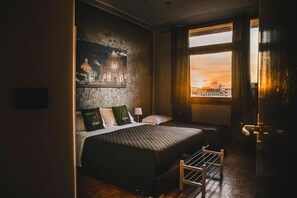 A room with a bed, a nightstand, a window with curtains, and a wall with a cityscape painting. - ALTA DIMORA b&b suites (Catania)