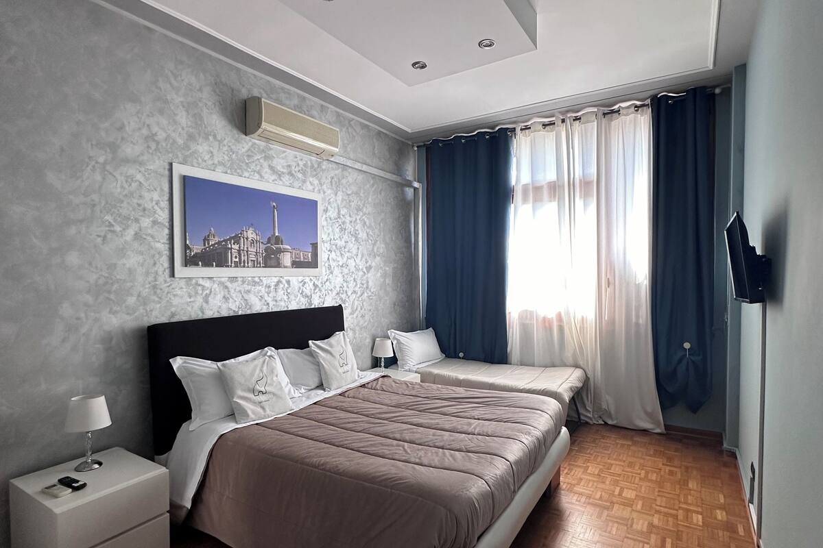 Ein modernes Schlafzimmer mit einem großen Bett, einem Nachttisch, einer Wandaircondition und einem Fenster mit Vorhängen.