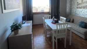 A dining area with a table and chairs, a small side table with a plant, a sofa with cushions, and a window with curtains. - ALTA DIMORA b&b suites (Catania)