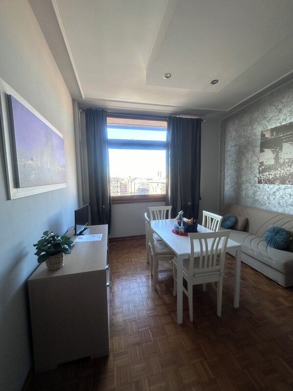 A dining area with a table and chairs, a small side table with a plant, a sofa with cushions, and a window with curtains. - ALTA DIMORA b&b suites (Catania)