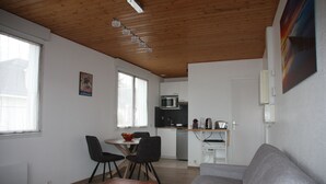 Ett modernt vardagsrum med ett träpanelat tak, en grå soffa, ett träbord och en matplats med bord och stolar.