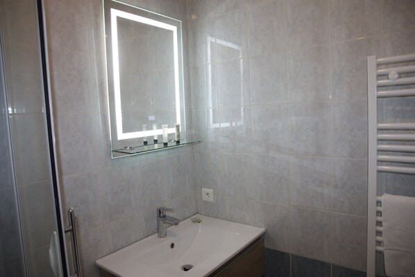 Une salle de bain avec un lavabo blanc, une étagère en verre au-dessus et un miroir avec un éclairage intégré.