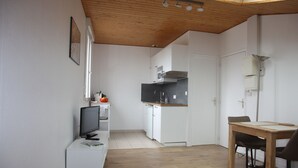 Ett kompakt kök med vita skåp, ett träbord och en tv som står på ett vitt tv-bord.