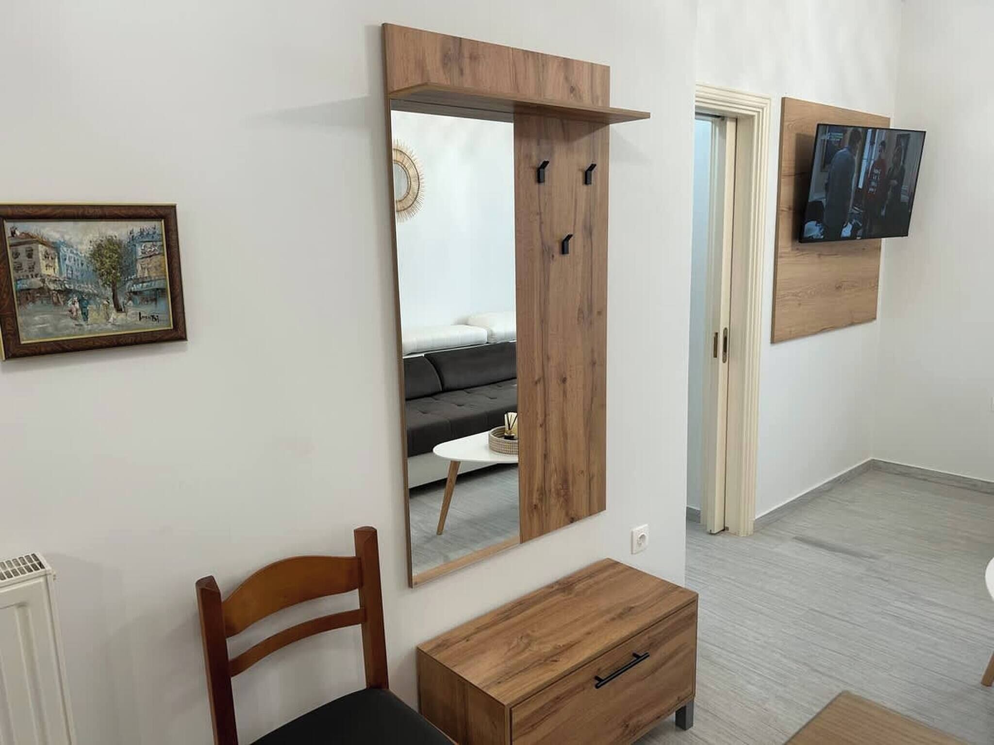 A modern living room with a large mirror, a wooden cabinet, a sofa, and a television mounted on the wall.