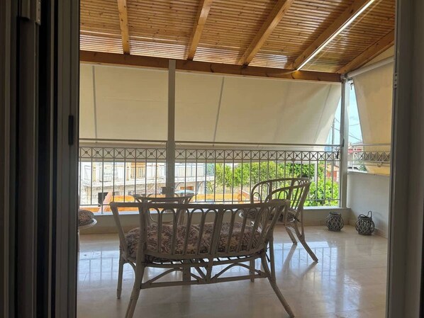 Un patio couvert avec une table et des chaises, donnant sur la rue, et un balcon agrémenté d’une balustrade.