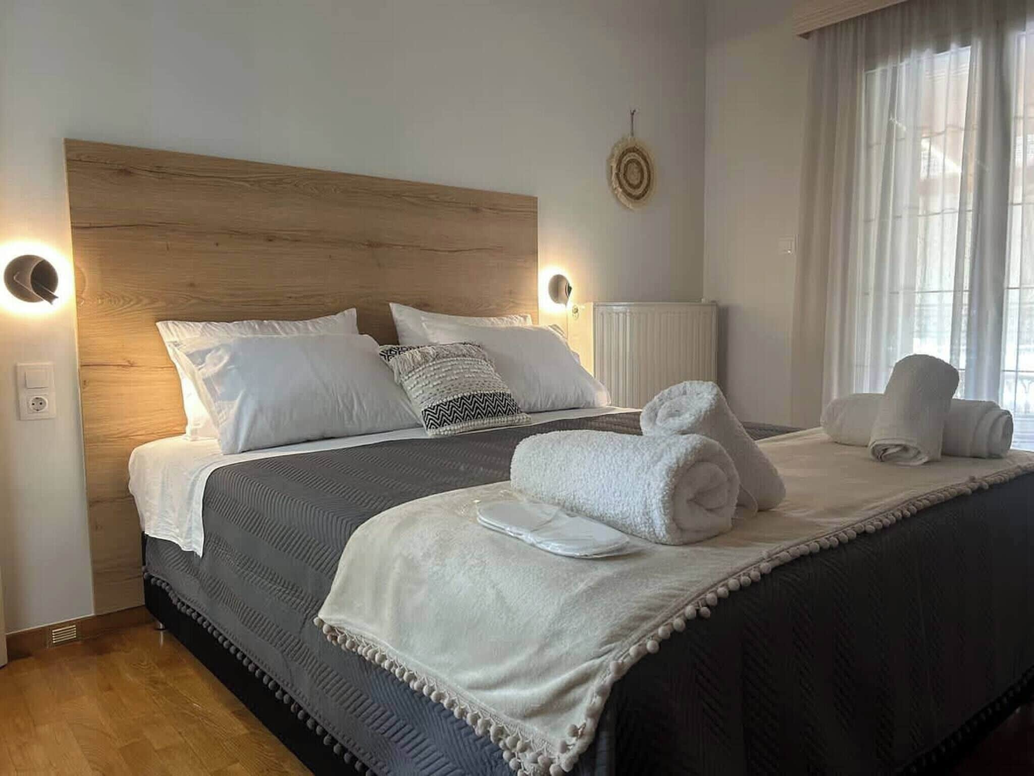 A neatly made bed with white linens and a grey bedspread, a bedside lamp, and a wall-mounted light fixture.