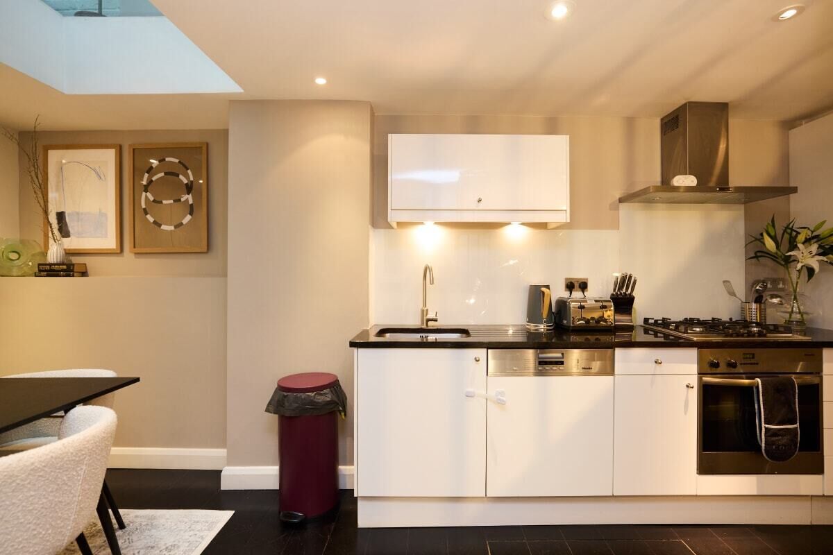 Una cocina moderna con armarios blancos, una campana extractora de acero inoxidable y un horno empotrado.