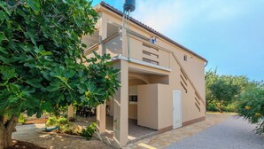 A two-story building with a covered outdoor seating area, a staircase, and a gravel driveway. - Apartment Zilic (Vir)