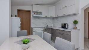 A modern kitchen with white cabinets, a built-in microwave, and a dining table with chairs. - Apartment Zilic (Vir)