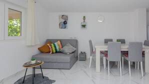 A modern living room with a grey sofa, a dining table with chairs, a small side table, and a window with curtains. - Apartment Zilic (Vir)
