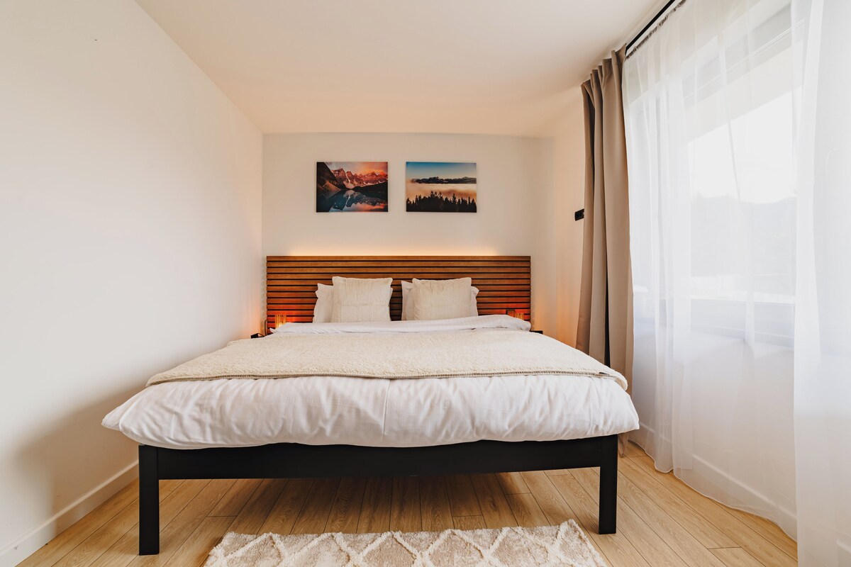 A neatly made bed with a wooden headboard, a white comforter, and two pillows. There are two framed pictures on the wall above the bed.
