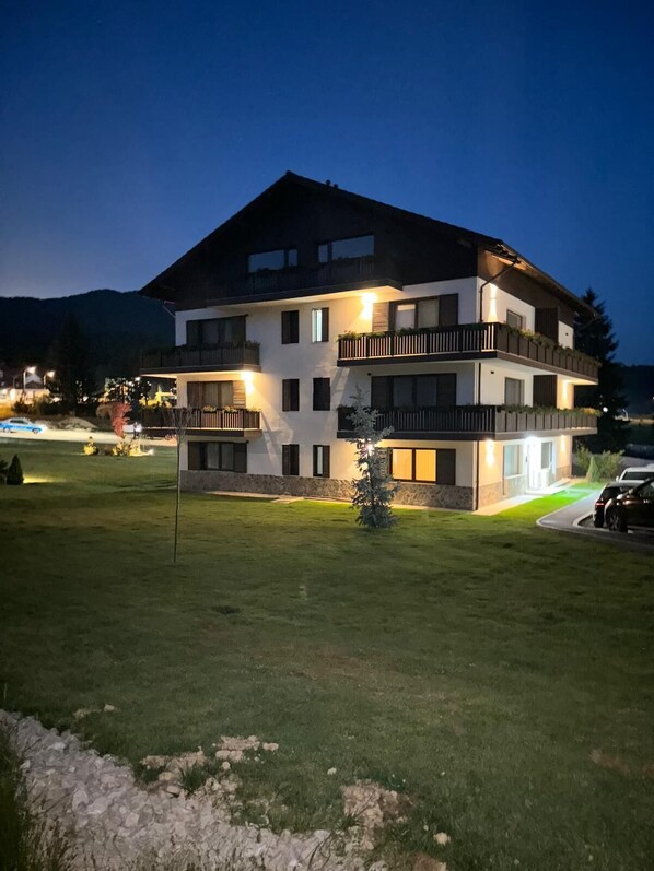 A multi-story building with balconies, a well-maintained lawn, and a mountain backdrop. - Albert Residence Grand Chalet (Brasov)
