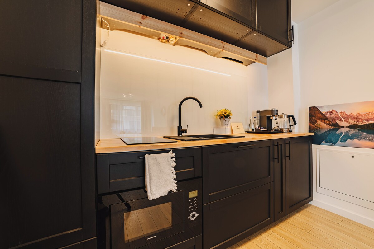 A modern kitchen with dark cabinetry, a wooden countertop, a black sink, and a coffee maker.