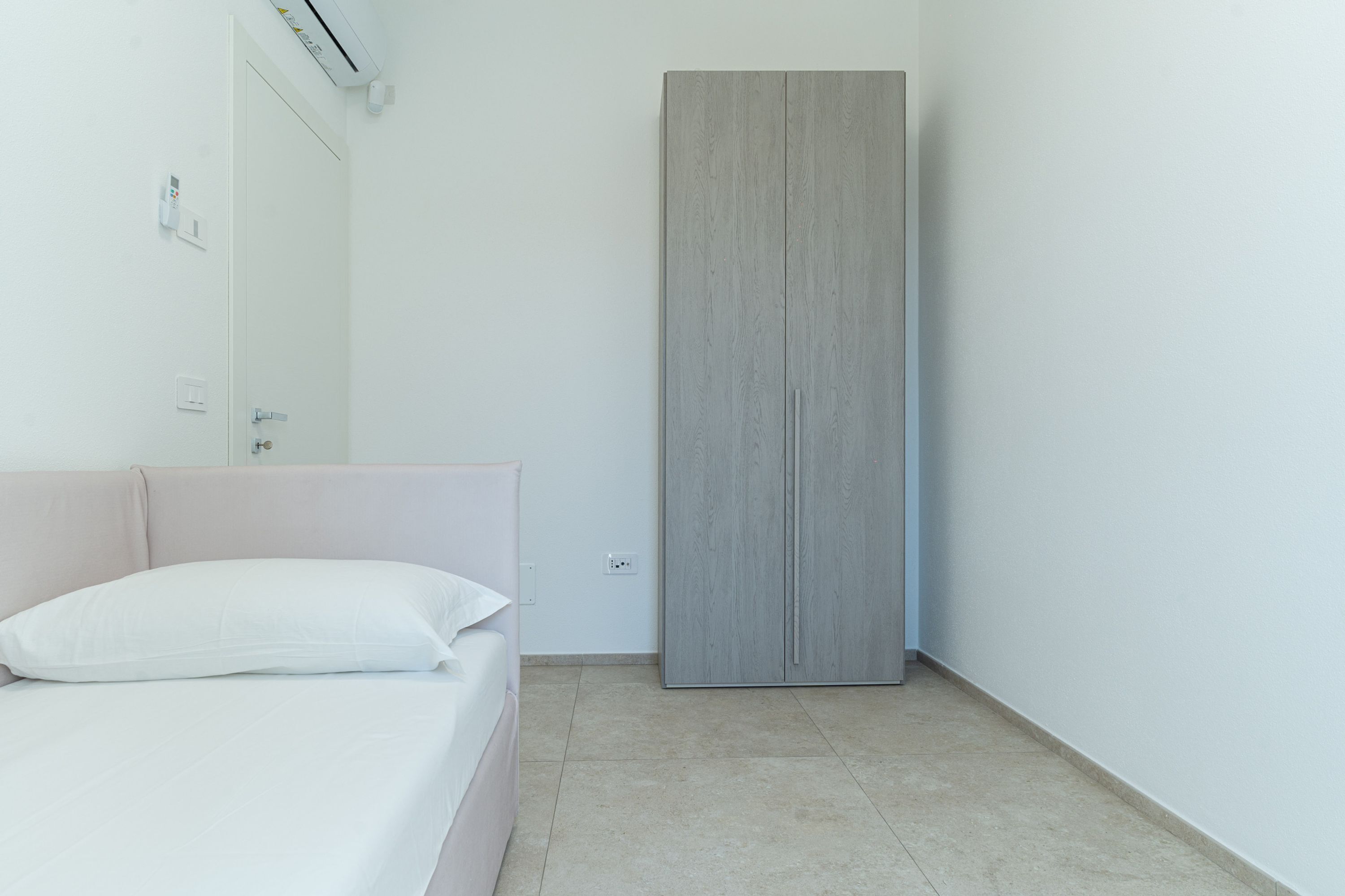 A bedroom with a bed, a wardrobe, and a wall-mounted air conditioner.
