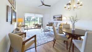 Ein geräumiges Wohnzimmer mit einem großen Esstisch, bequemen Sitzmöglichkeiten, einem Deckenventilator und Blick durch große Schiebeglastüren auf einen Außenbereich.