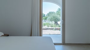 Een slaapkamer met een bed, een raam met gordijnen en uitzicht op een tuin en bomen.