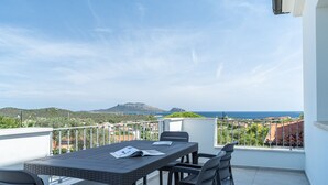 A balcony with a table and chairs, overlooking a coastal landscape with hills and the sea. - Appartamento La Perla by Wonderful Italy (Olbia)