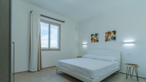 A bedroom with a bed, a window with curtains, and two wall-mounted artworks. - Appartamento La Perla by Wonderful Italy (Olbia)