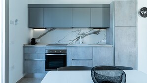 A modern kitchen with grey cabinets, a marble backsplash, and a built-in oven. - Appartamento La Perla by Wonderful Italy (Olbia)