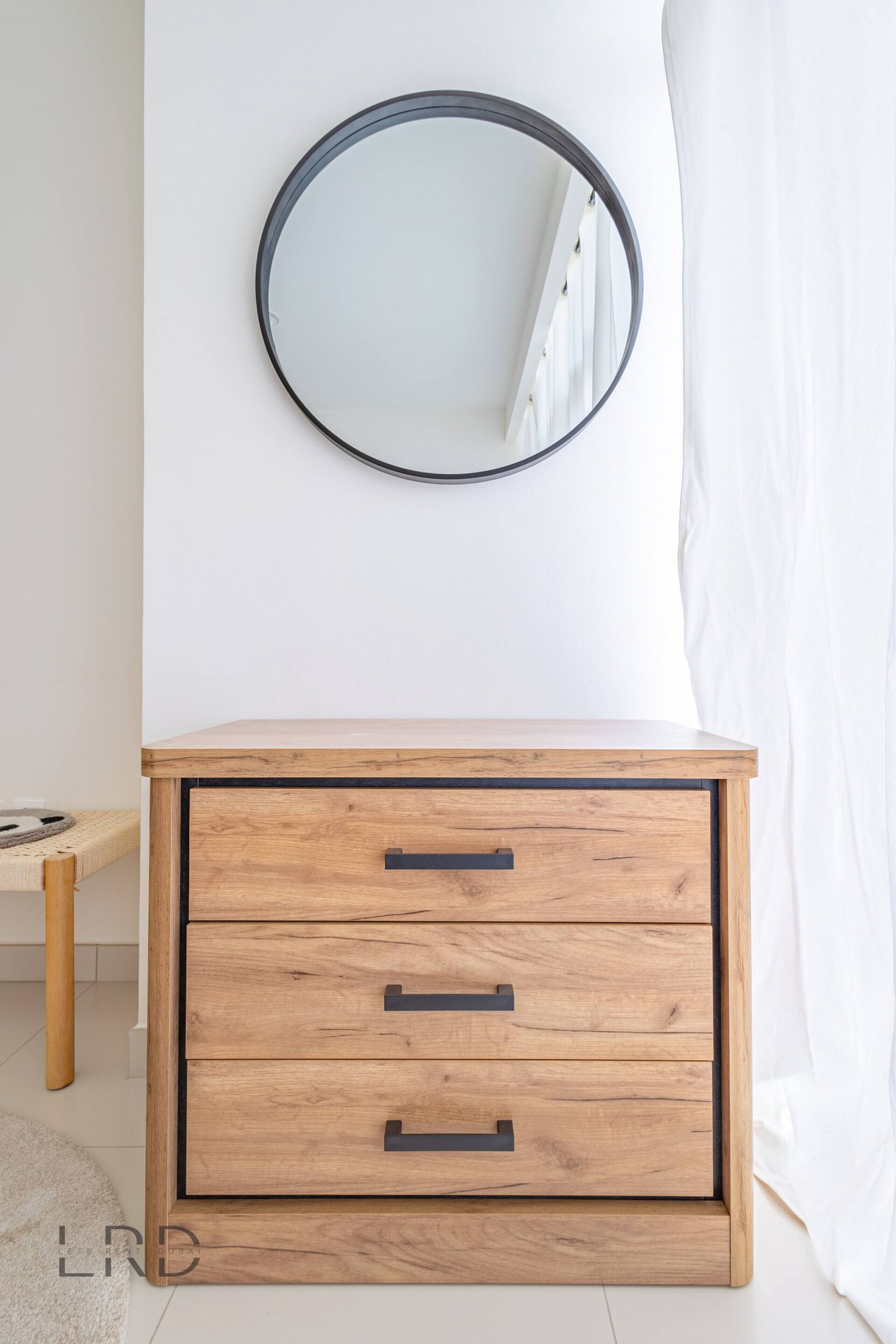 A wooden cabinet with three drawers and a round mirror above it.