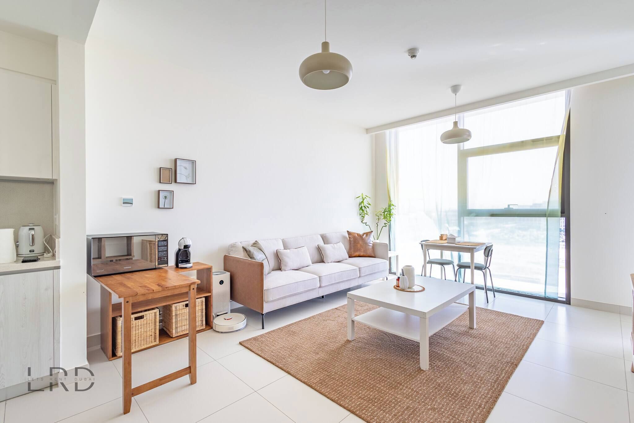 Un salon moderne avec un canapé, une table basse et une table à manger. Il y a également un coin cuisine équipé d’un four à micro-ondes et d’une bouilloire. La pièce est dotée de grandes fenêtres et offre une vue sur la ville.