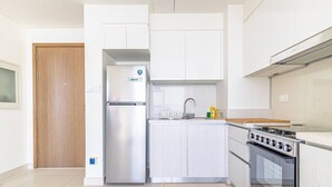 Eine moderne Küche mit weißen Schränken, einem Edelstahlkühlschrank, einem Gasherd und einer Holztür.