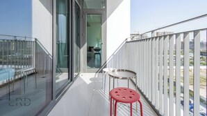Ein Balkon mit Glastür zu einem Zimmer, einem kleinen Tisch und einem roten Hocker.