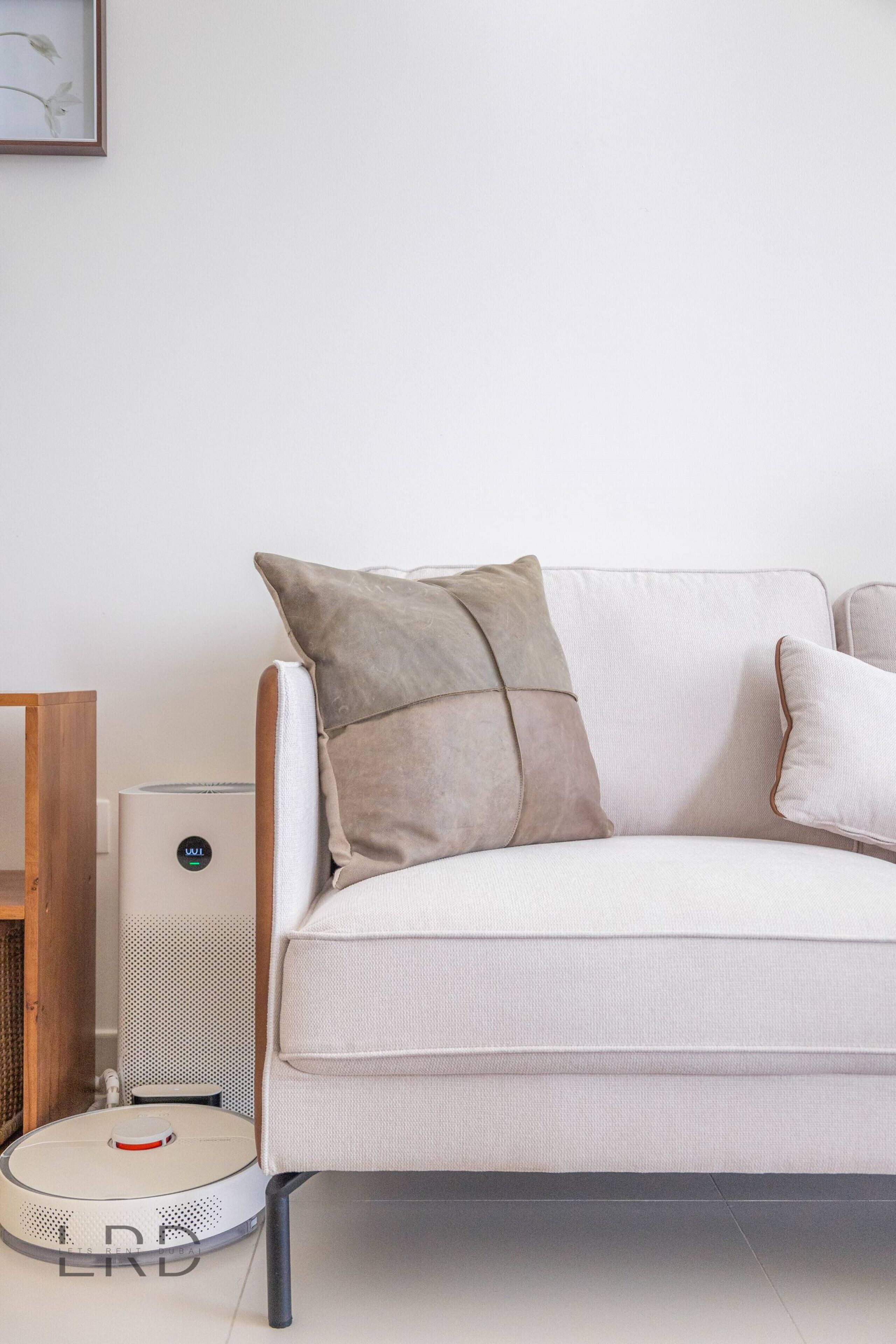 Una sala de estar moderna con un sofá blanco, dos almohadas, una mesita y un robot aspirador.