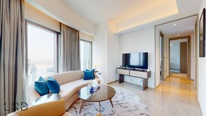 A modern hotel room with a sofa, a coffee table, a flat-screen TV, and a large window offering a city view. - Classy & Cozy 2BR Harbour Point (Dubai)