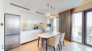 A modern kitchen with white cabinets, a Bosch refrigerator, and a dining area with a marble table and four chairs. - Classy & Cozy 2BR Harbour Point (Dubai)