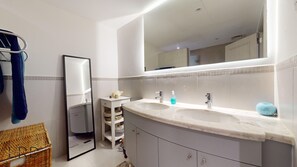 A bathroom with a large mirror, two sinks, and a small shelf with toiletries.