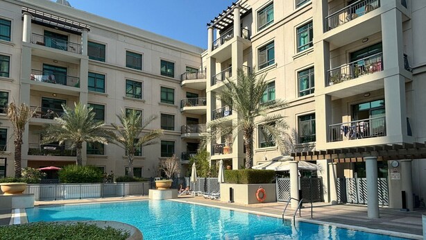 Una piscina rodeada por un edificio de varios pisos con balcones y palmeras.