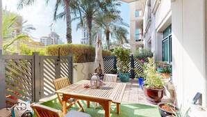 Un patio con mesa y sillas de madera, rodeado de plantas en macetas y un pequeño jardín.