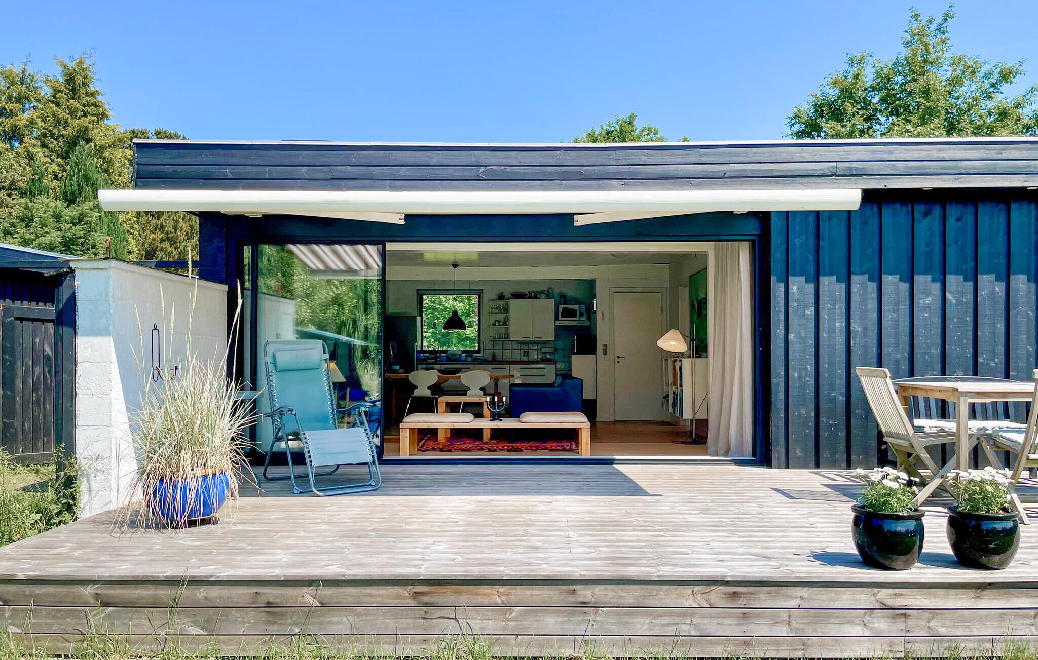 Ein modernes Haus mit einer Terrasse, einem Essbereich und einer durch die offene Tür einsehbaren Küche.