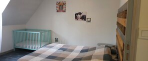 A room with a crib, a bed with a checkered blanket, and two framed pictures on the wall. - Villa with a private heated pool in Normandy (Treis-Sants-en-Ouche)
