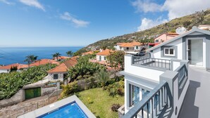 A residential area with a swimming pool, houses with red-tiled roofs, and a view of the sea.