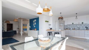 A modern kitchen with white cabinets, a blue backsplash, and a dining area with a glass table and white chairs.