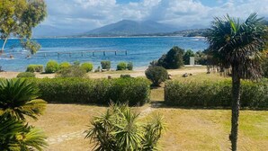 A coastal view with a clear sky, a wooden pier extending into the sea, and a mountain in the background.