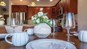 Una mesa de comedor dispuesta con platos blancos, vasos y un jarrón decorativo con flores blancas.