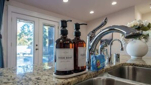 Una cocina con encimera de granito, pileta de acero inoxidable y dos botellas de lavavajillas.