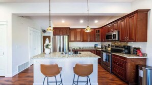 Una cocina moderna con armarios de madera, electrodomésticos de acero inoxidable y una isla central con taburetes de bar.