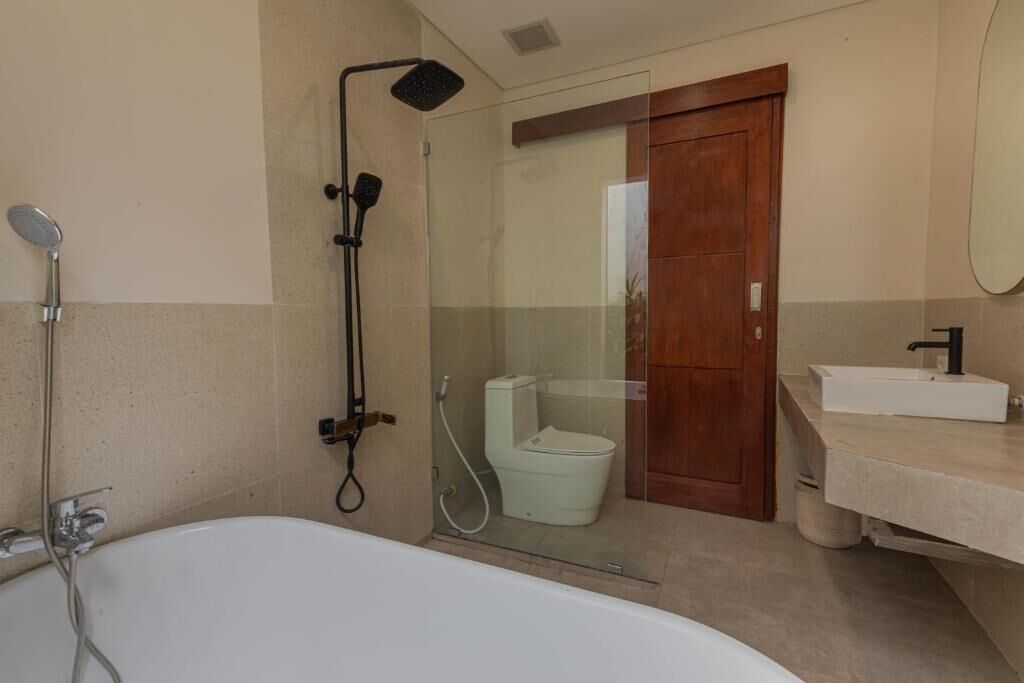 Un baño con ducha envuelta en vidrio, una bañera blanca y una puerta de madera.