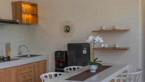 A compact kitchen with wooden cabinets, a built-in sink, a black refrigerator, and a dining area with white chairs and a central table. - Jobon Villas  (Ungasan)