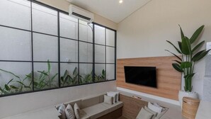 A modern living room with a large window, a flat-screen TV mounted on the wall, and a seating area with cushions. - Jobon Villas  (Ungasan)