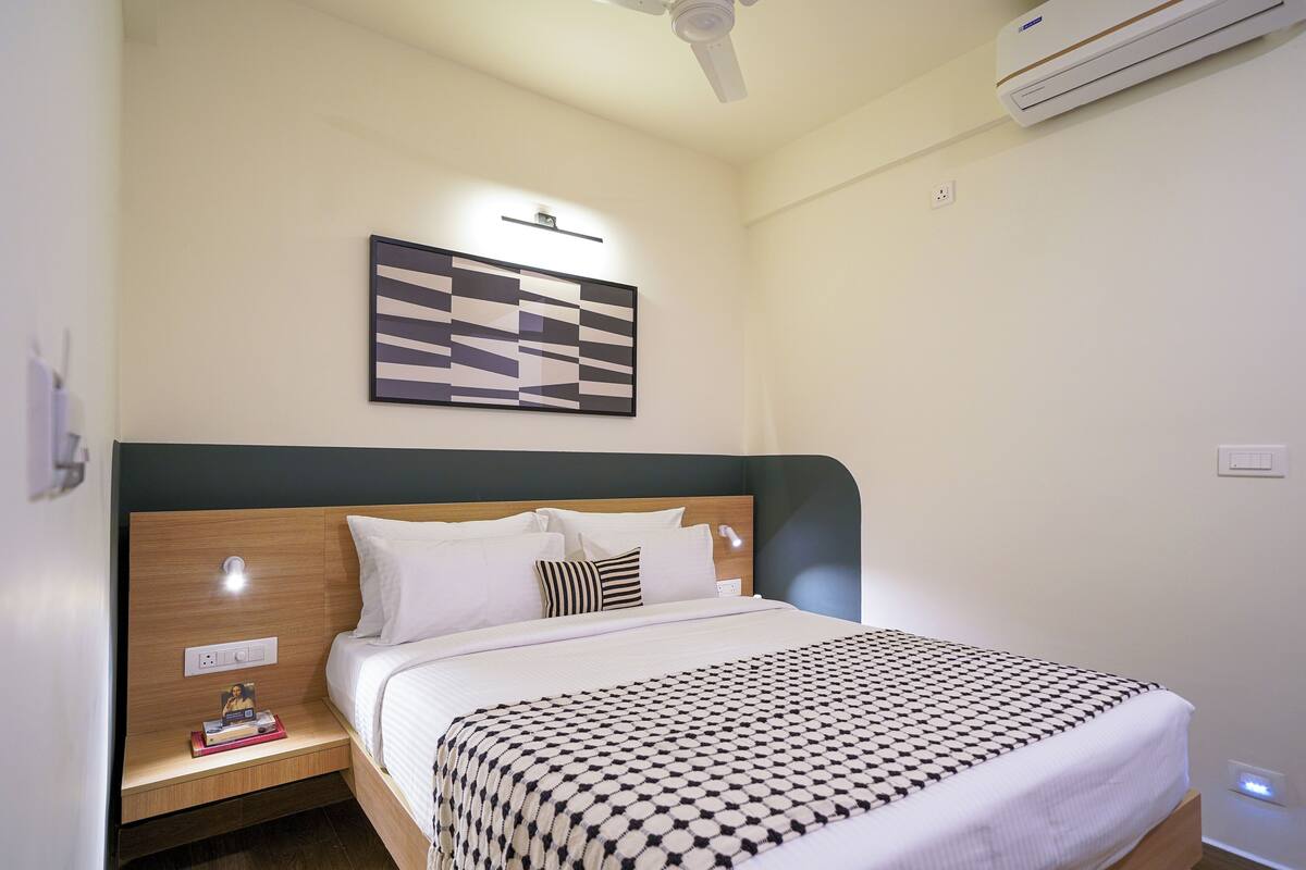 A neatly made bed with a patterned bedspread, a bedside table with a lamp, and a wall-mounted artwork.