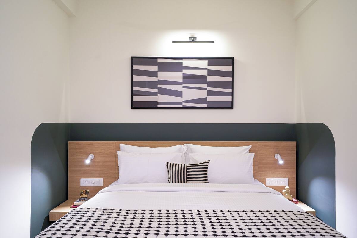 A modern hotel room with a neatly made bed, a wall-mounted artwork, and bedside lamps.