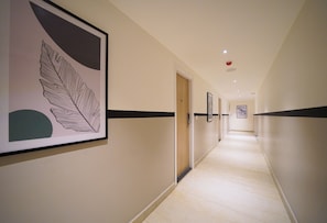 A long, narrow hallway with a light-colored floor and walls, featuring a framed artwork on the left and a door at the end.